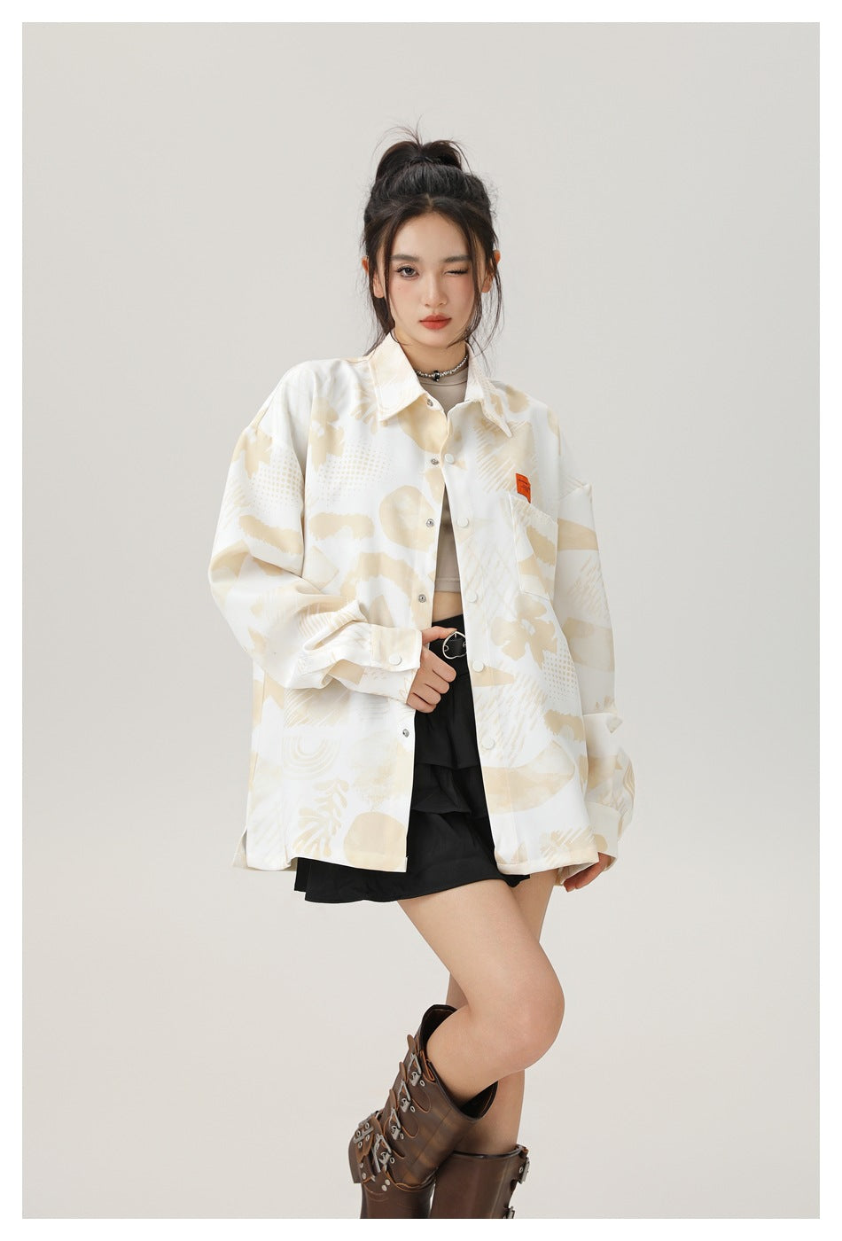 Closer front view of a model wearing a cream and beige abstract-print shirt jacket with snap buttons and a chest pocket.