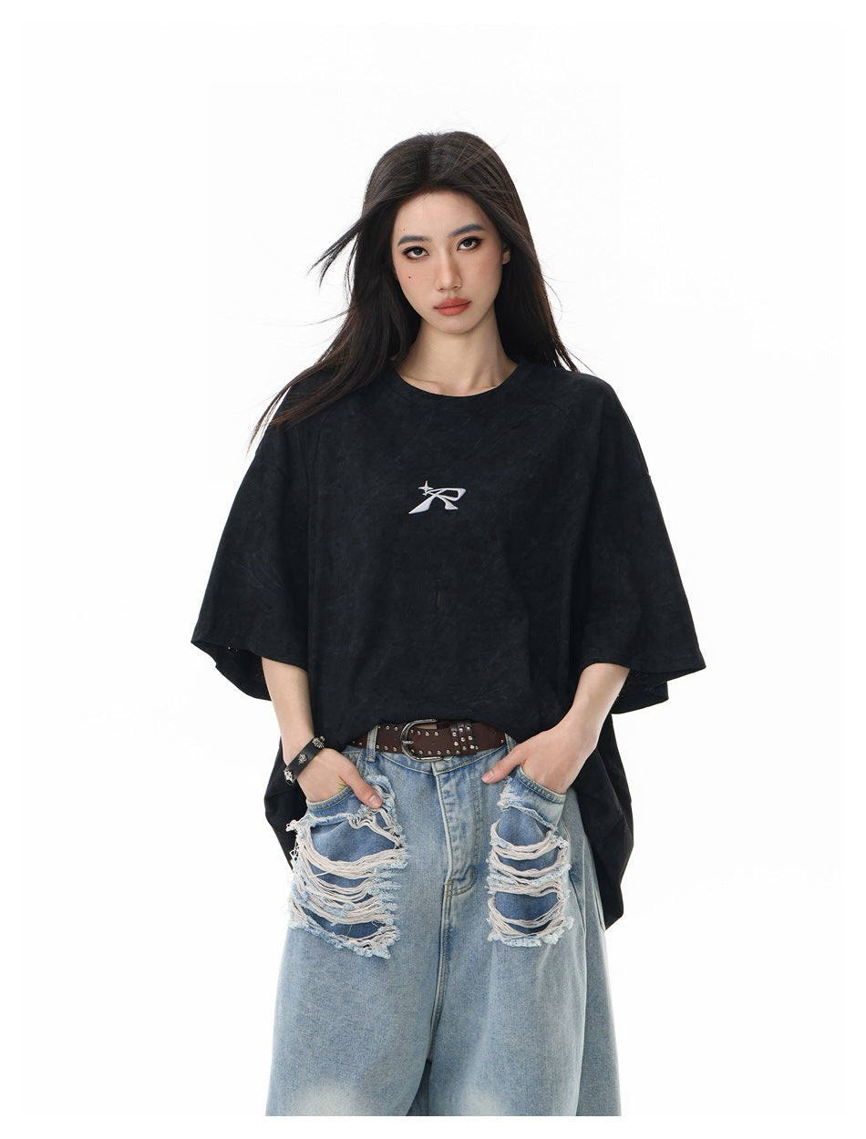 Front view of a model in an oversized black T-shirt with a small white chest emblem and ripped light-wash jeans.