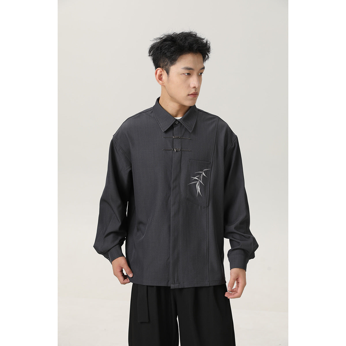 Man wearing a charcoal gray long-sleeve shirt with metal front fasteners and a bamboo-embroidered chest pocket, with black