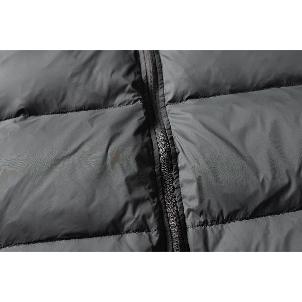 Close-up of a charcoal puffer jacket's central zipper and horizontal quilted sections.