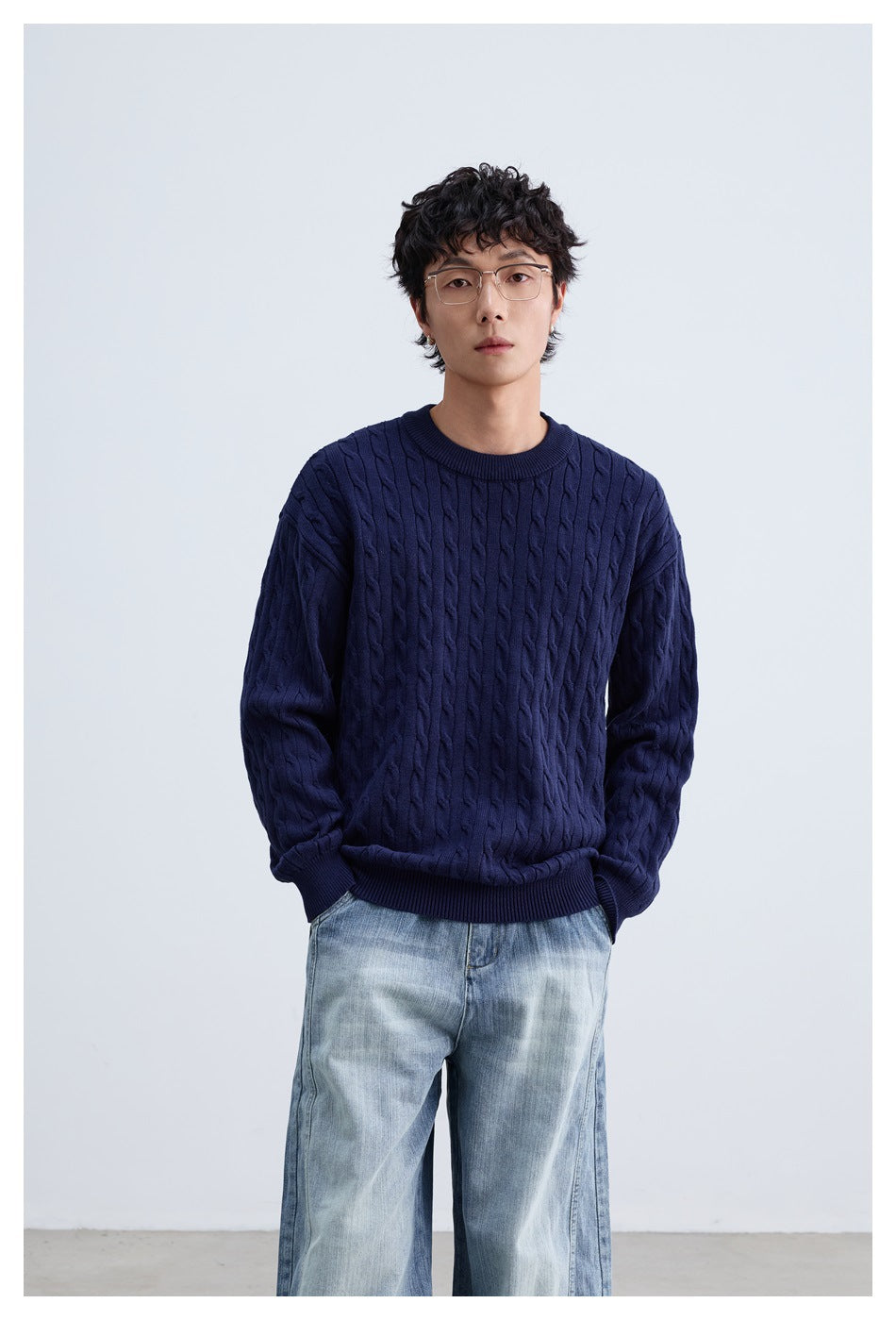 Model wearing a navy cable-knit crewneck sweater with light-wash jeans.