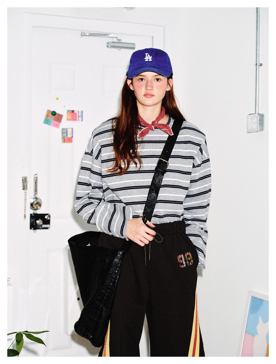 Person wearing gray striped long-sleeve top with blue cap, red bandana, black shoulder bag and black pants