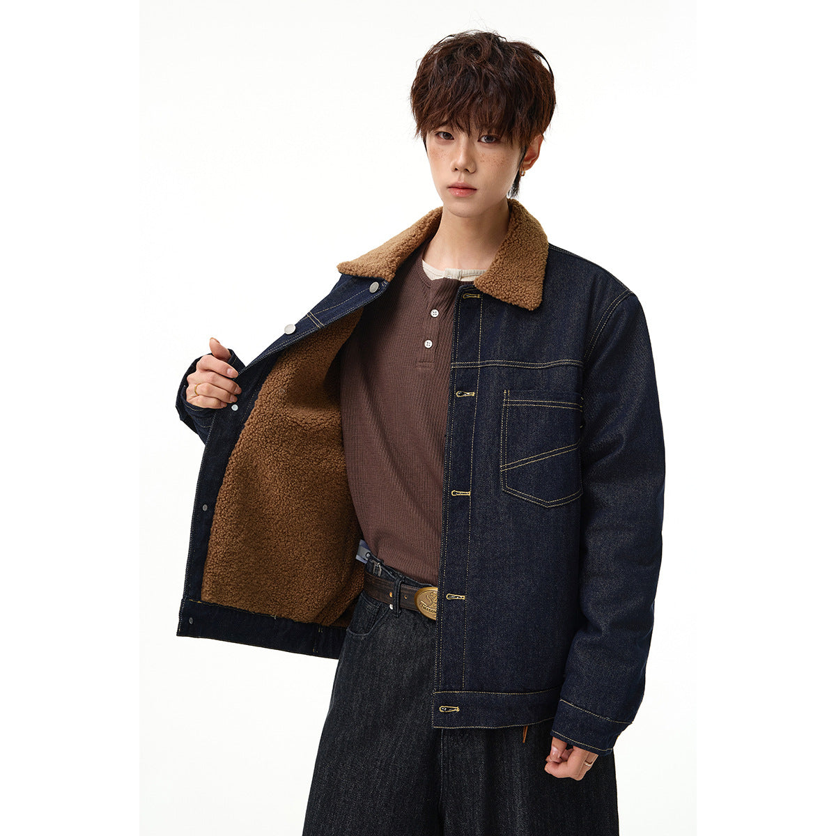 Model wearing an open dark indigo denim jacket with a tan sherpa collar and lining, showing its single chest pocket.