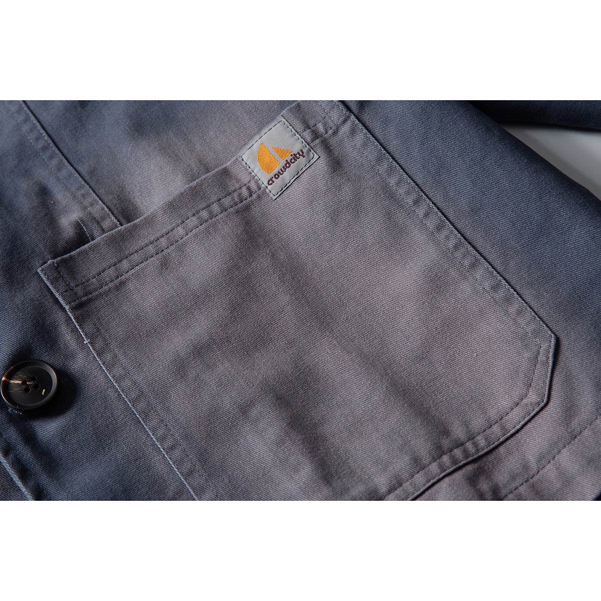 Close-up of a gray jacket’s large chest pocket and small sewn logo patch.