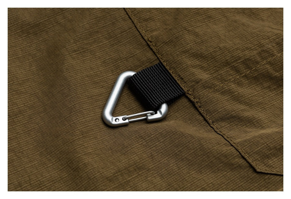 Close-up of a silver carabiner attached by a black fabric loop to an olive-brown jacket.