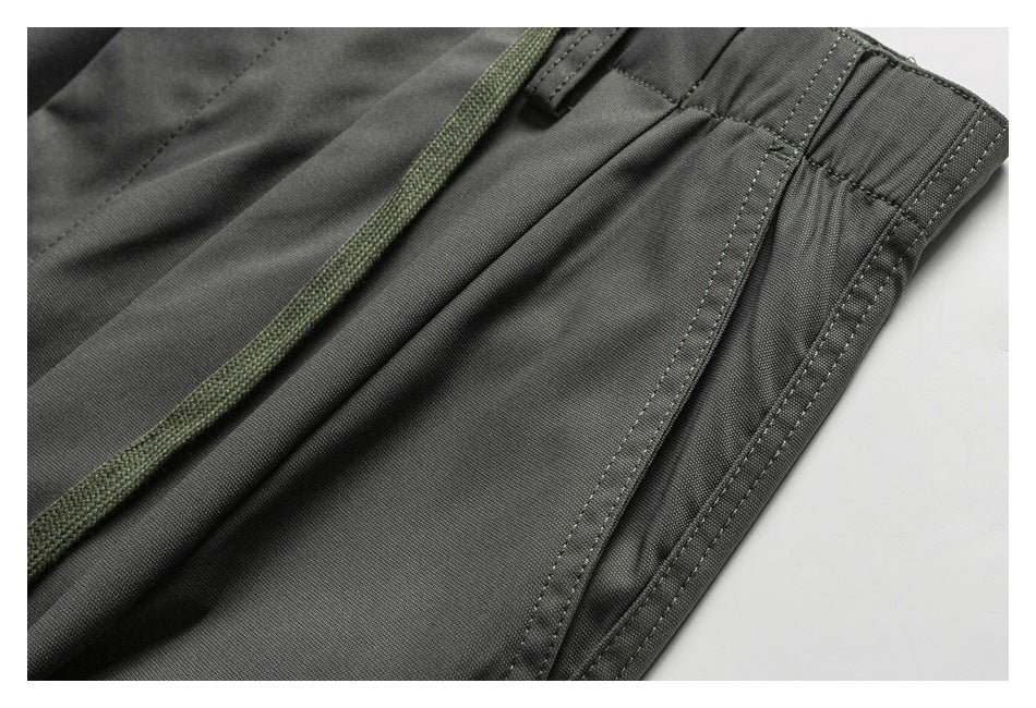 Close-up of charcoal trousers showing the waistband, belt loop, drawstring, and side seam.