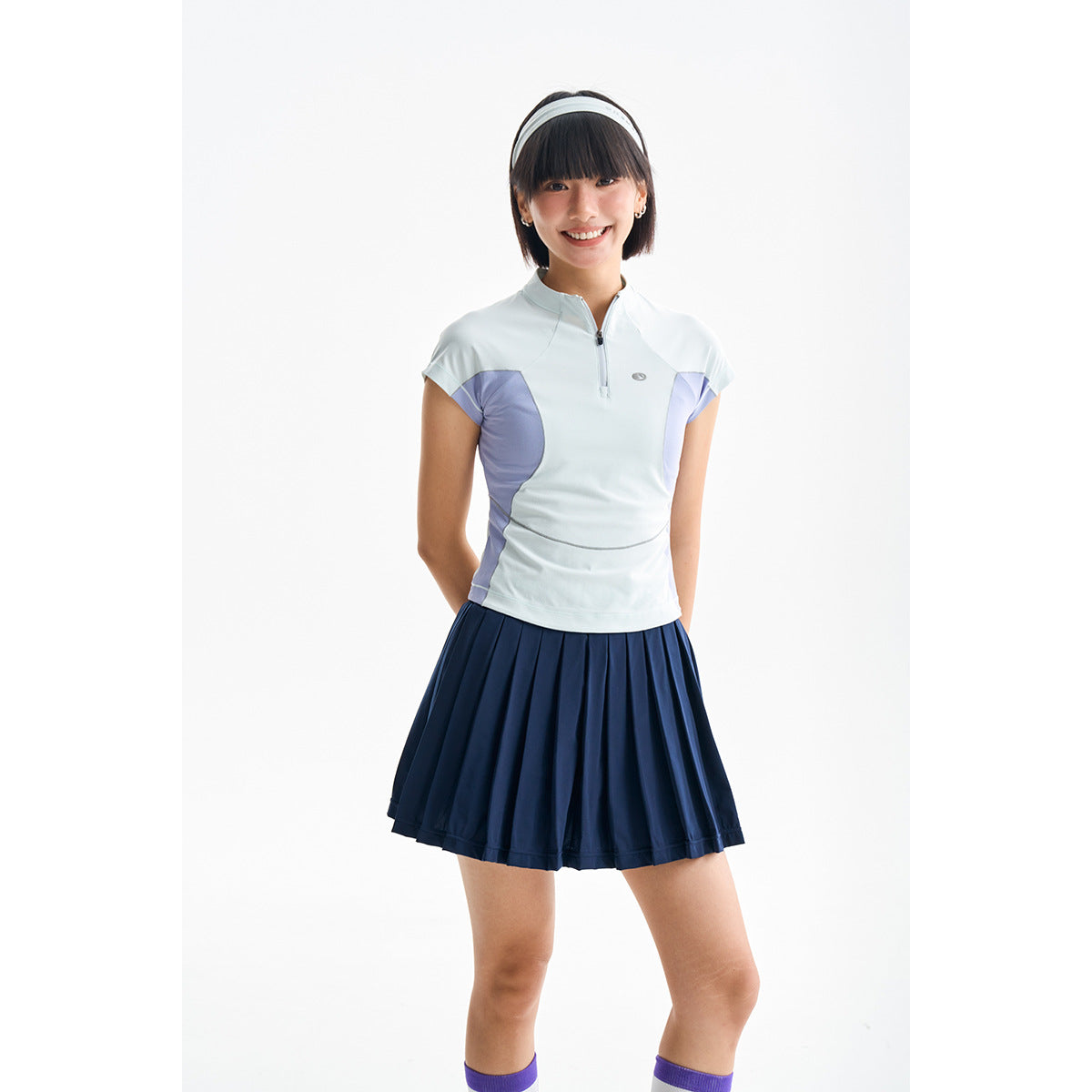 Model wearing a pale blue quarter-zip top with lavender panels and a navy pleated skirt.