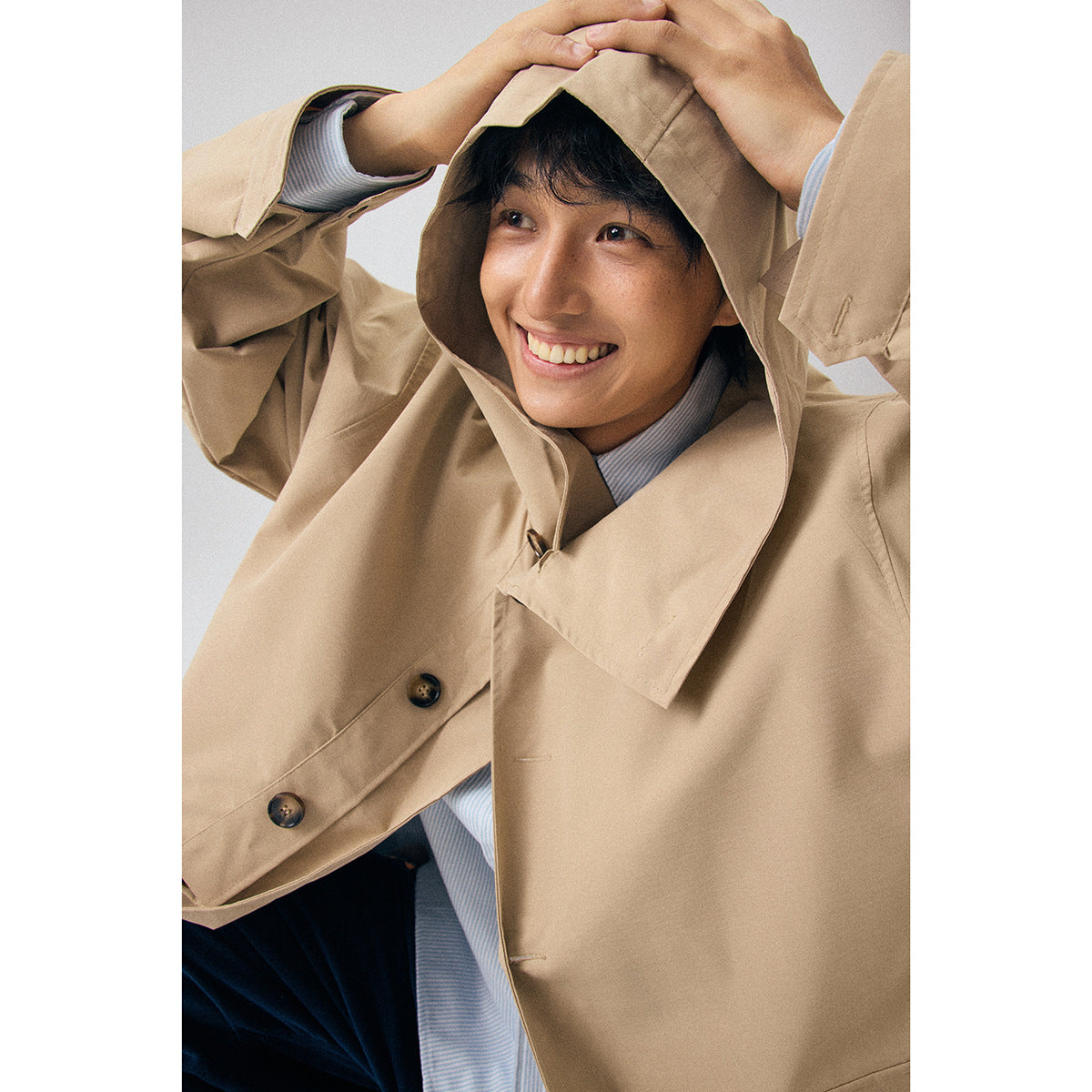 Close-up of a model wearing a beige hooded coat, showing its wide collar and dark buttons.