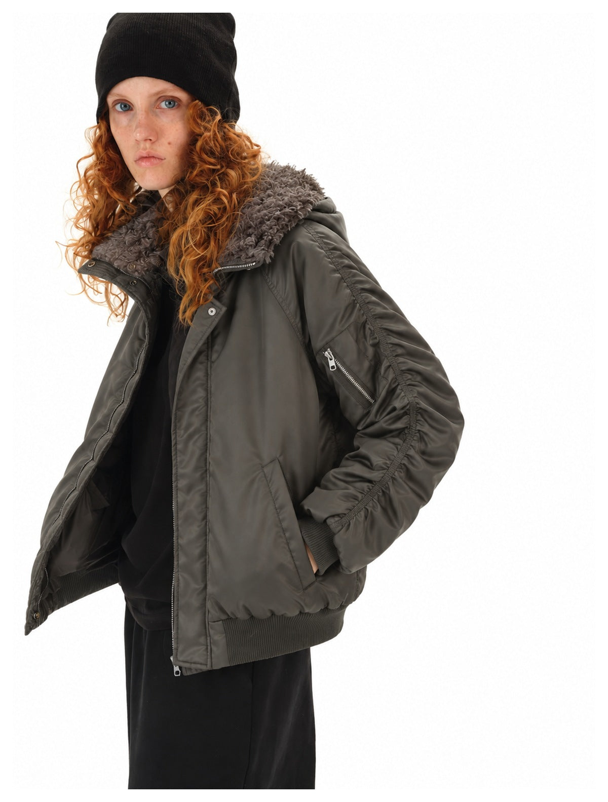 Model wearing a charcoal gray bomber jacket with a plush collar, zippered sleeve pocket, ribbed hem, and black beanie.
