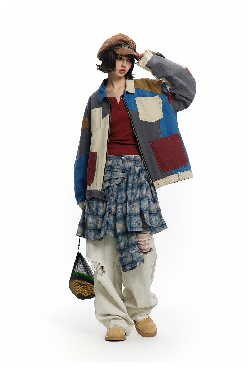 Model wearing a multicolor patchwork jacket, blue patterned wrap skirt, and loose cream trousers against a white background.