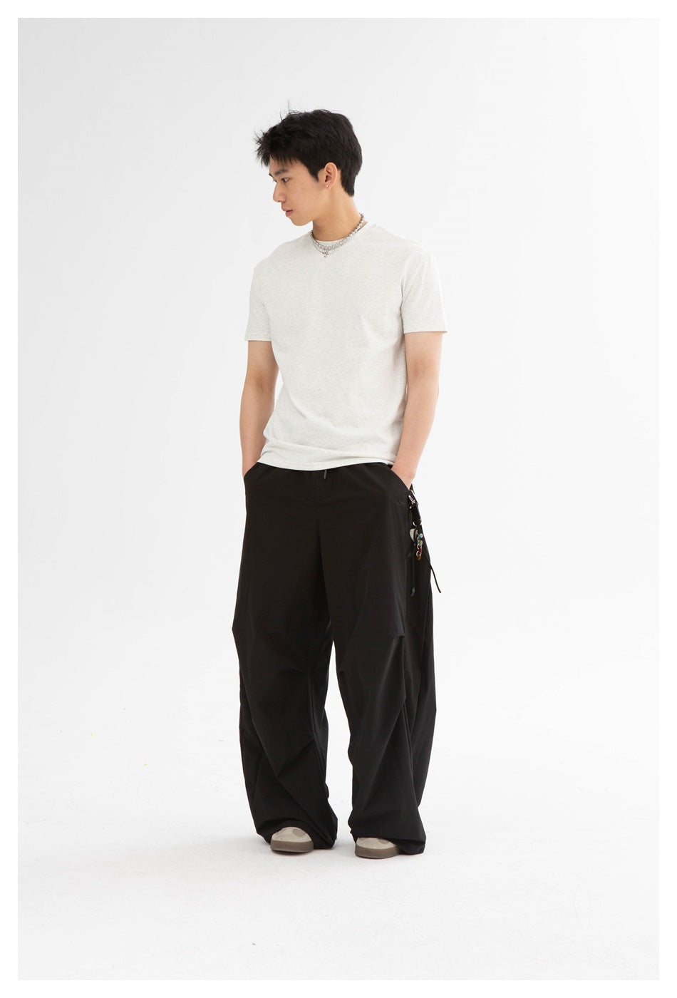 Model wearing a light heather-gray crew-neck T-shirt and wide black pants, looking to the side.