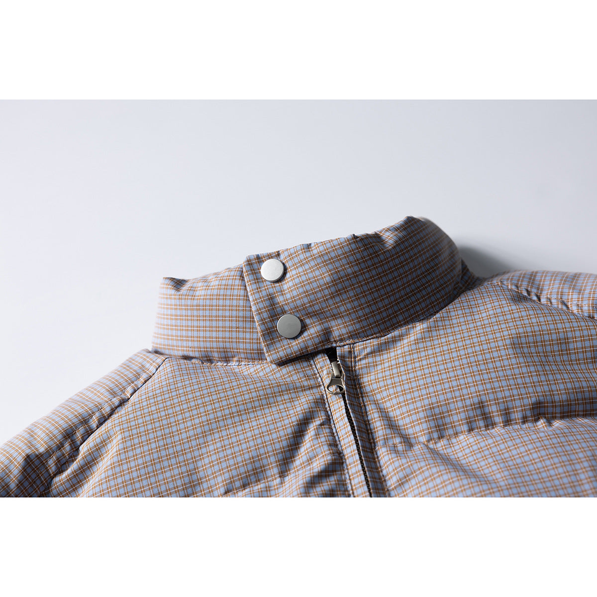 Close-up of a blue-gray and tan checked padded jacket collar with snap buttons and front zipper.