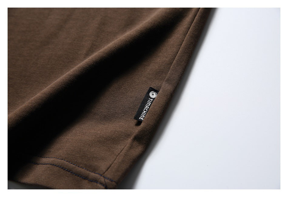 Close-up of a small black woven label sewn into the brown T-shirt near a stitched hem.