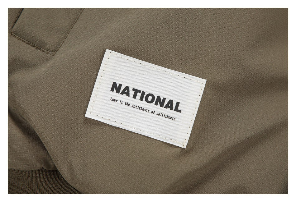 Close-up of a white sewn clothing label reading “NATIONAL” on taupe-brown fabric.
