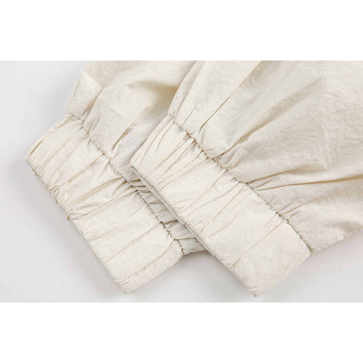 Close-up of gathered elastic cuffs and hems on overlapping ivory jacket sleeves.