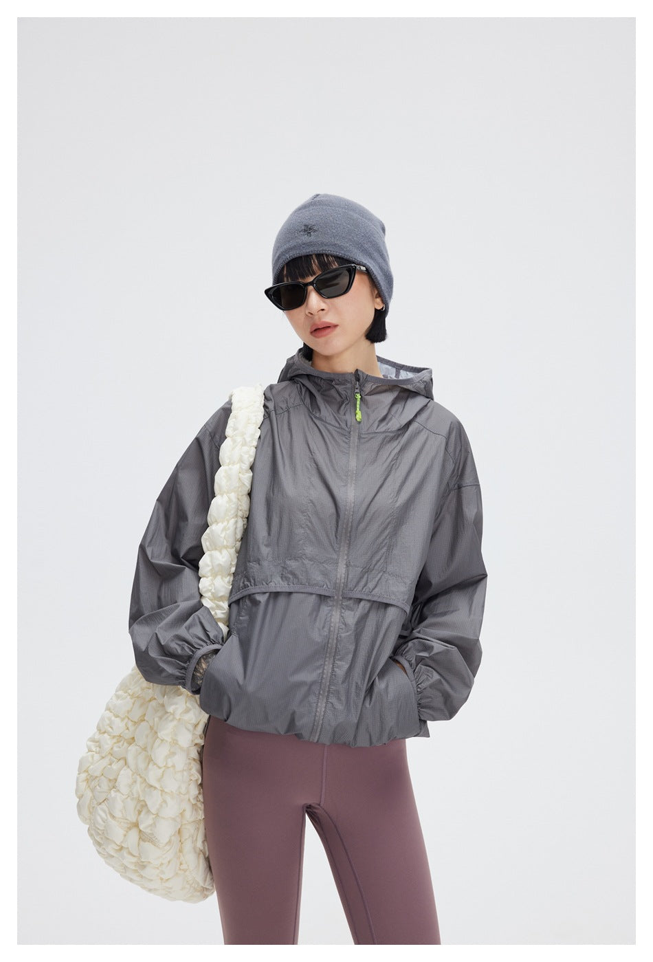 Closer front view of a model in a gray hooded windbreaker with a bright green zipper pull and mauve leggings.