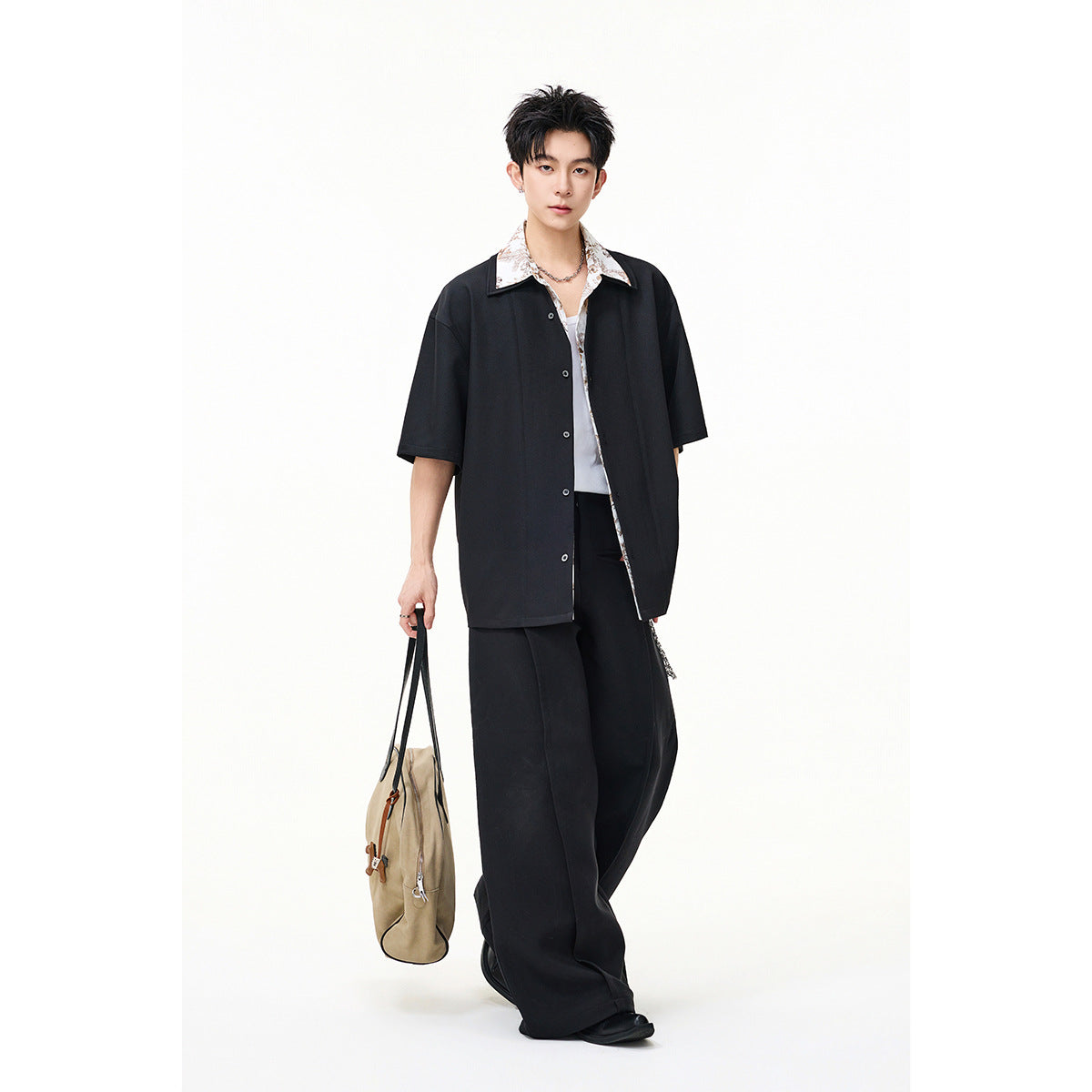 Model in a black short-sleeve button shirt layered over a white floral-collar top and wide black trousers.