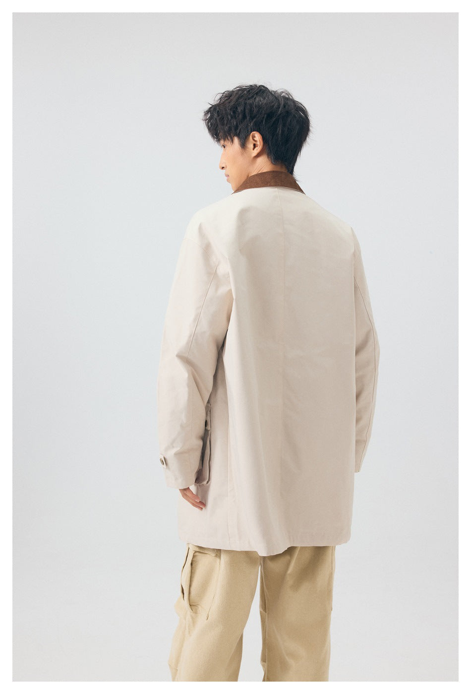 Back view of model wearing an off-white mid-length jacket with brown collar and beige pants