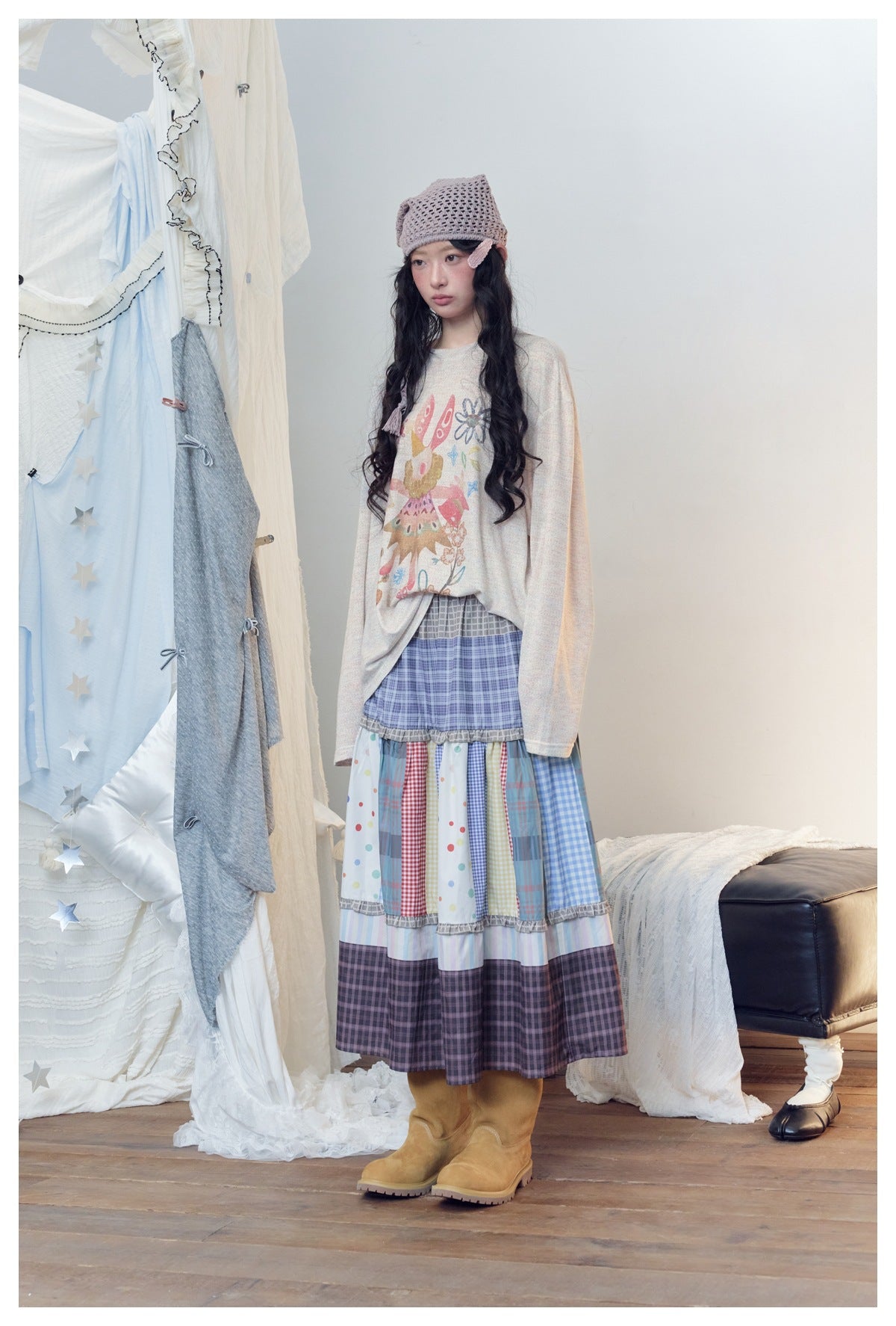 Model wearing a light oatmeal long-sleeve graphic top with a colorful print, a tiered patchwork skirt, and tan boots.