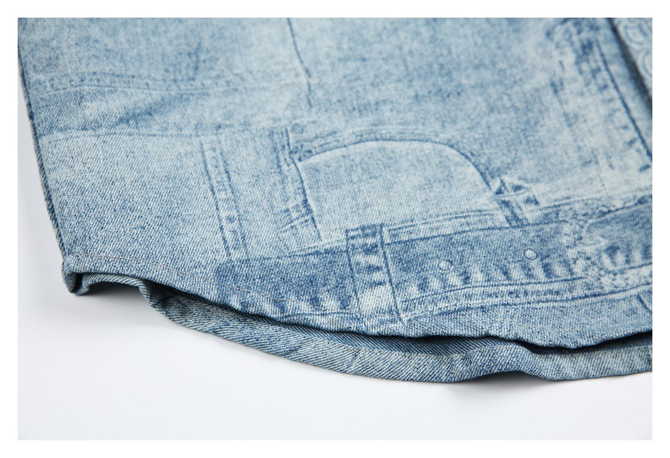 Close-up of a light blue denim garment hem with distressed patchwork-style printed graphics and stitching.