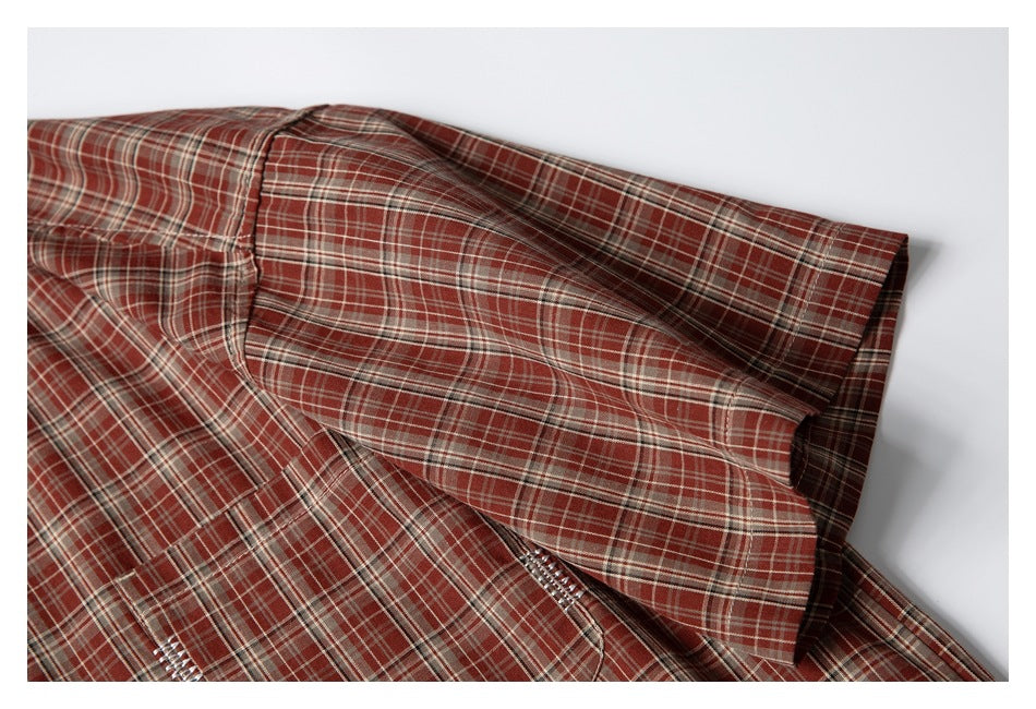 Close-up of the rust-red plaid shirt's short sleeve and shoulder seam on a white background.