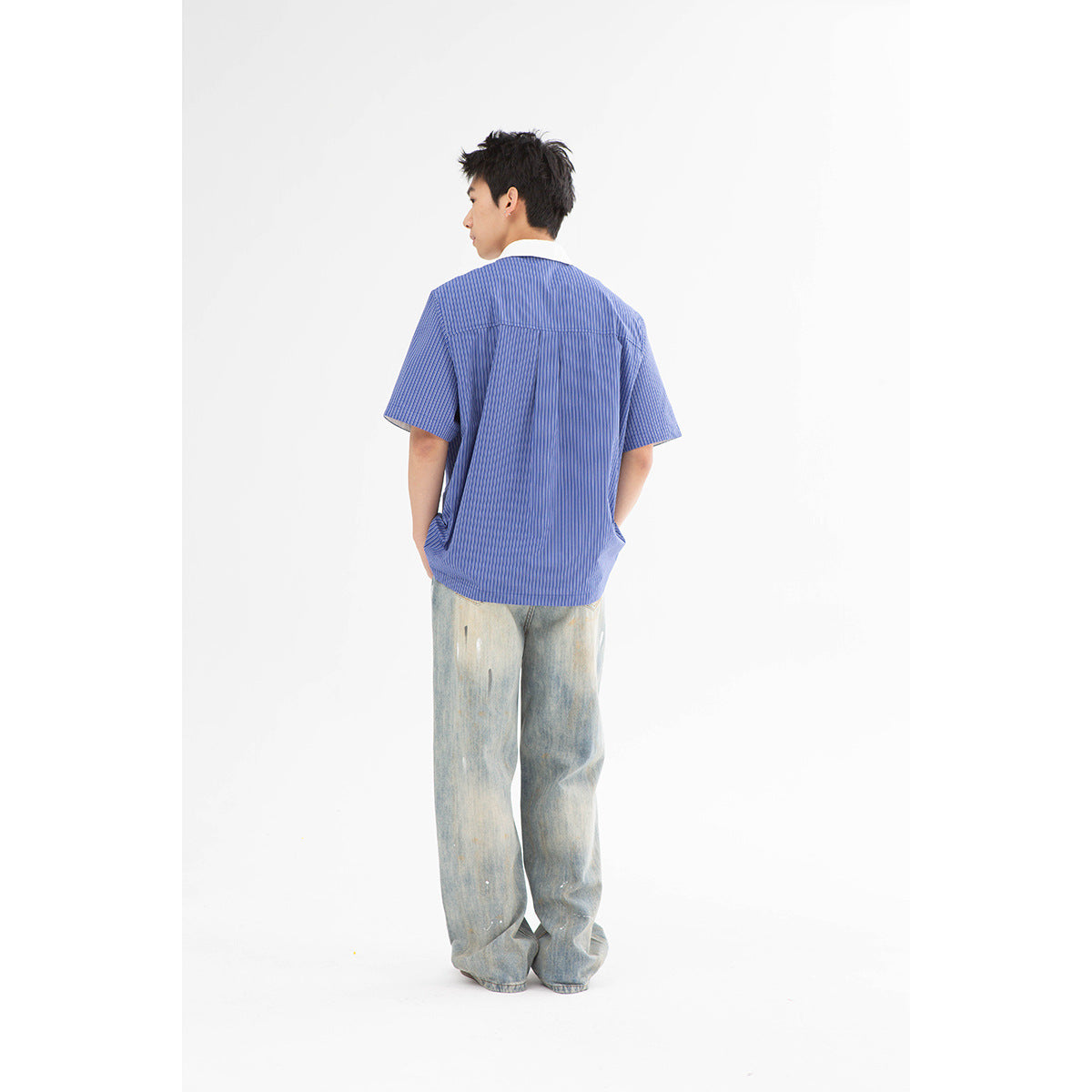 Rear view of a model wearing a blue pinstriped short-sleeve shirt with a white collar and loose light-wash jeans.
