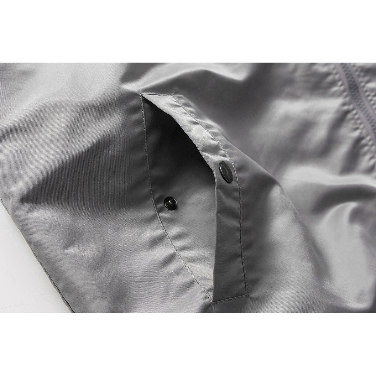 Close-up of a gray jacket pocket opening with a snap-button fastening.