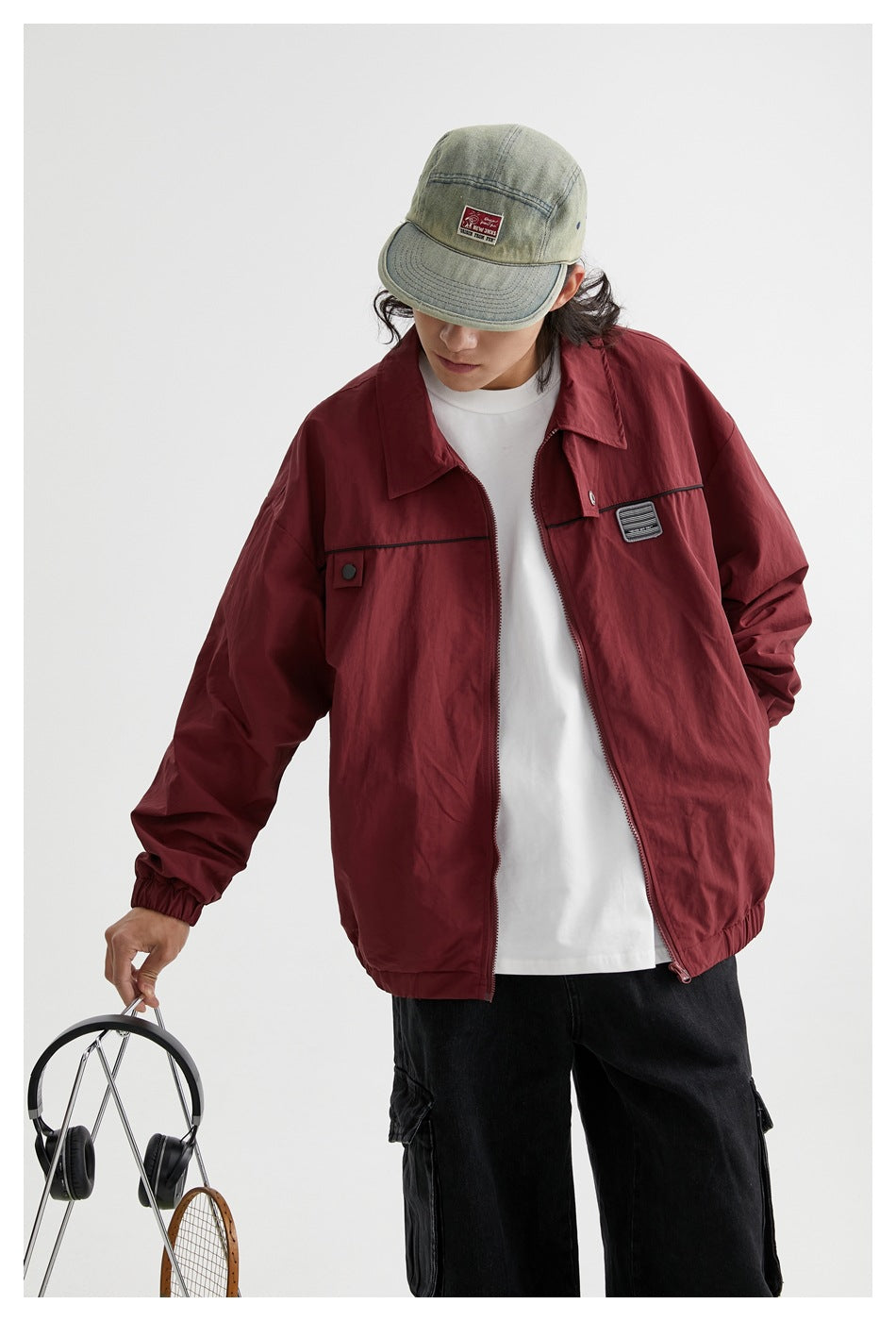 Closer view of a model wearing an open burgundy zip jacket with black chest trim over a white shirt.