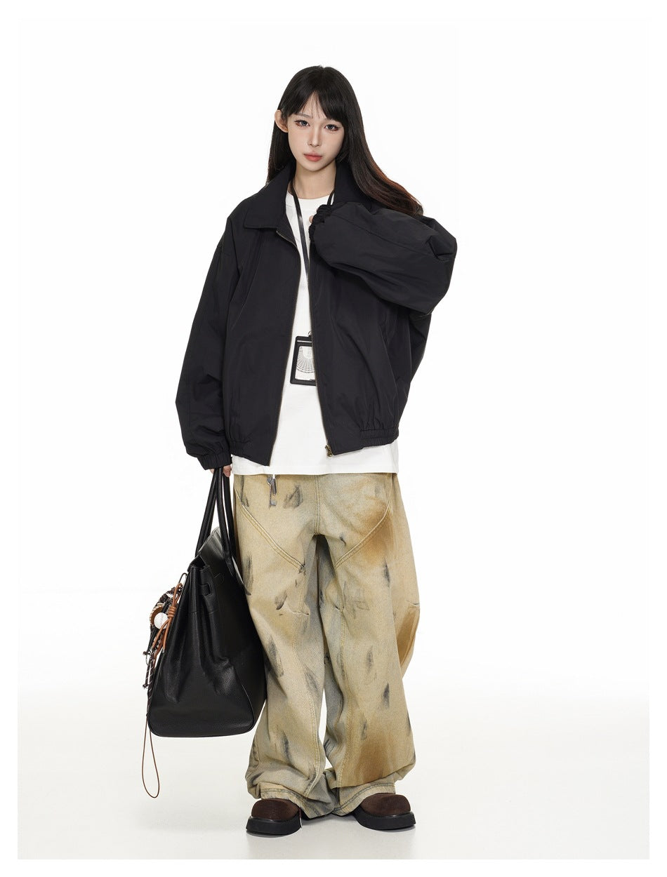 Model wearing a black zip jacket open over a white tee with wide-leg pants, one sleeve held out, carrying a black tote