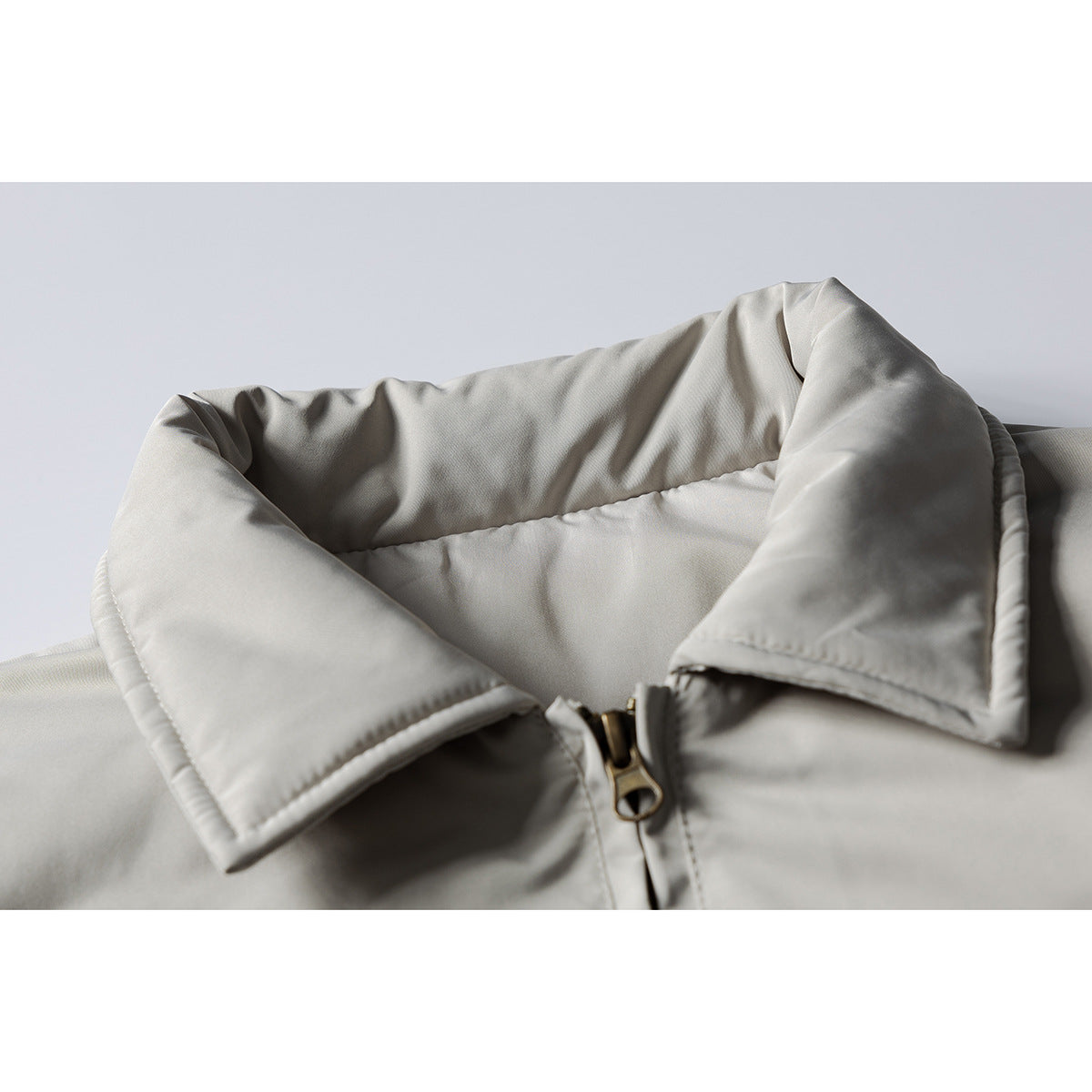 Close-up of a light gray jacket's padded collar and brass-tone front zipper.