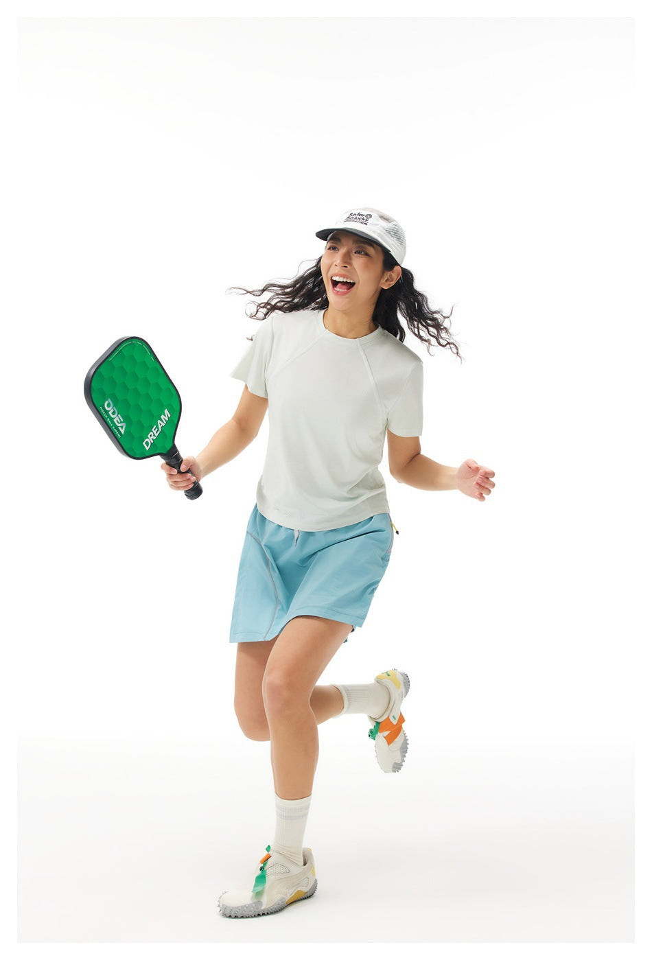 Model wearing an off-white short-sleeve shirt and light blue athletic skirt while holding a paddle.