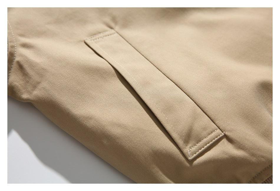 Close-up of a tan jacket's narrow welt pocket and stitched fabric panels.