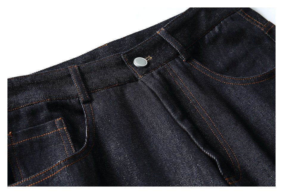 Close-up of dark indigo jeans showing the waistband, button, fly and front pocket with orange stitching.
