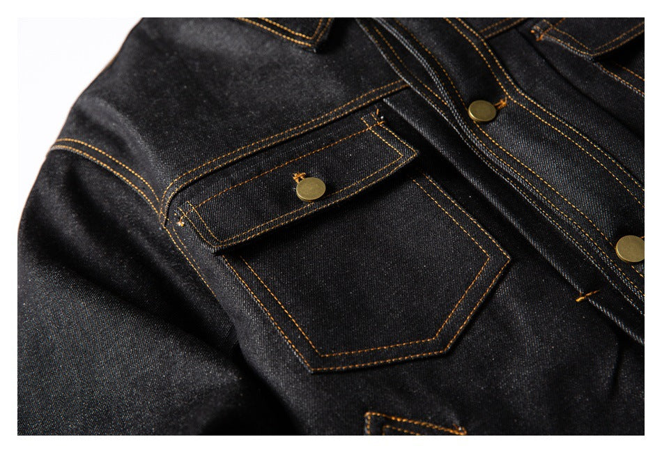 Close-up of a dark denim jacket chest pocket with a buttoned flap and golden contrast stitching.