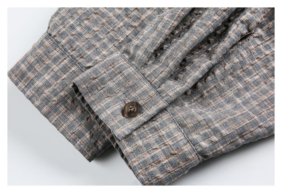 Close-up of the gray-brown plaid shirt cuff with a dark button and gathered sleeve fabric.
