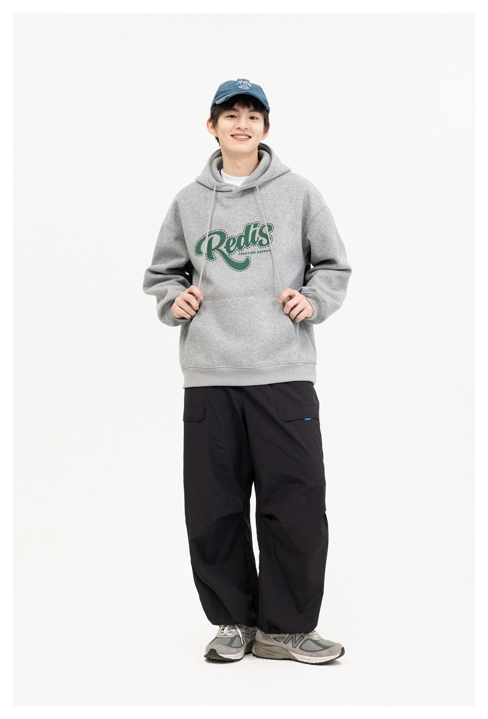 Smiling model wearing a gray hoodie with a green chest graphic and black cargo pants.
