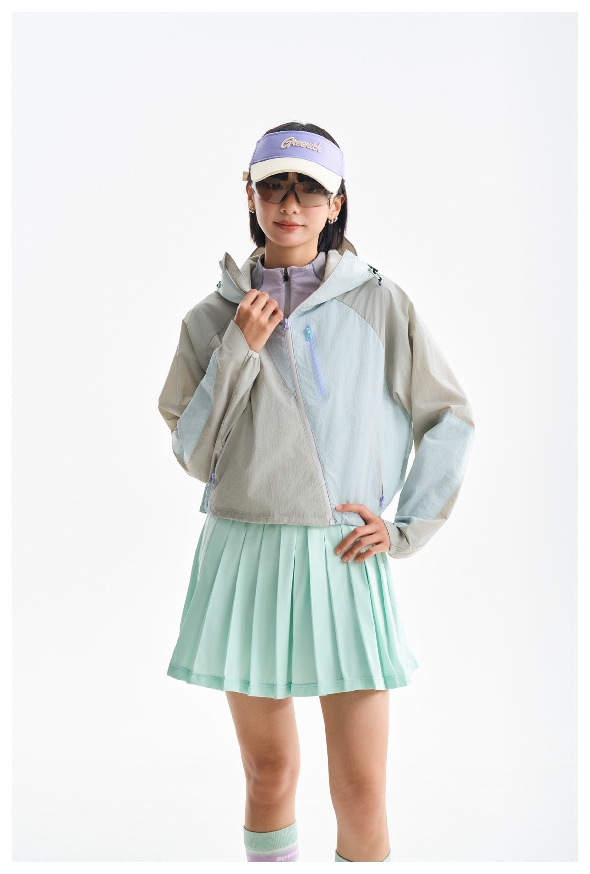 Model wearing a pale gray and mint color-block hooded zip jacket with pastel zippers and a mint pleated skirt.