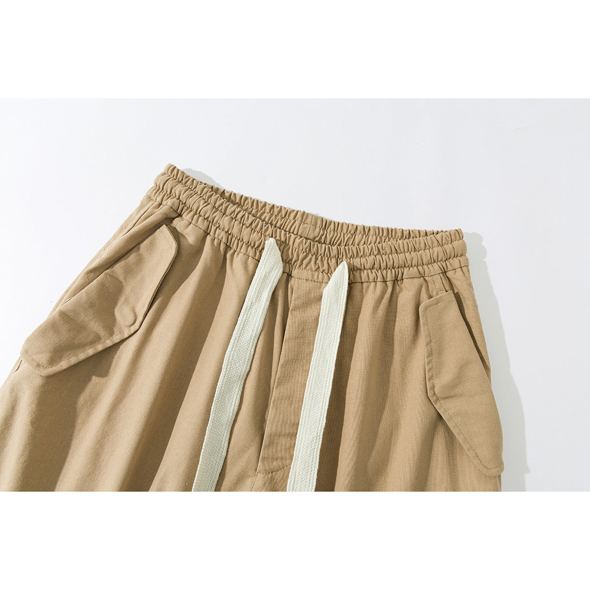 Close-up of tan pants showing an elastic waistband, white drawstrings, and angled flap pockets.