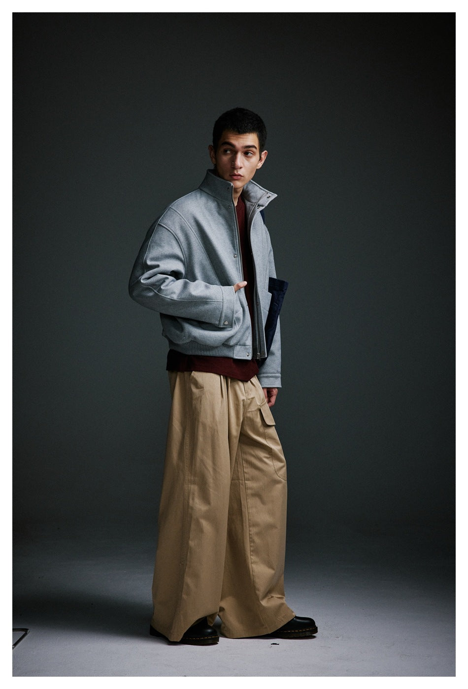 Model wearing a light gray stand-collar jacket and burgundy shirt with wide beige trousers.