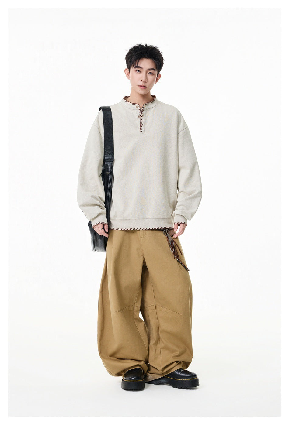 Full-length model wearing a light beige oversized pullover with contrast-stitched trim and loose tan trousers.