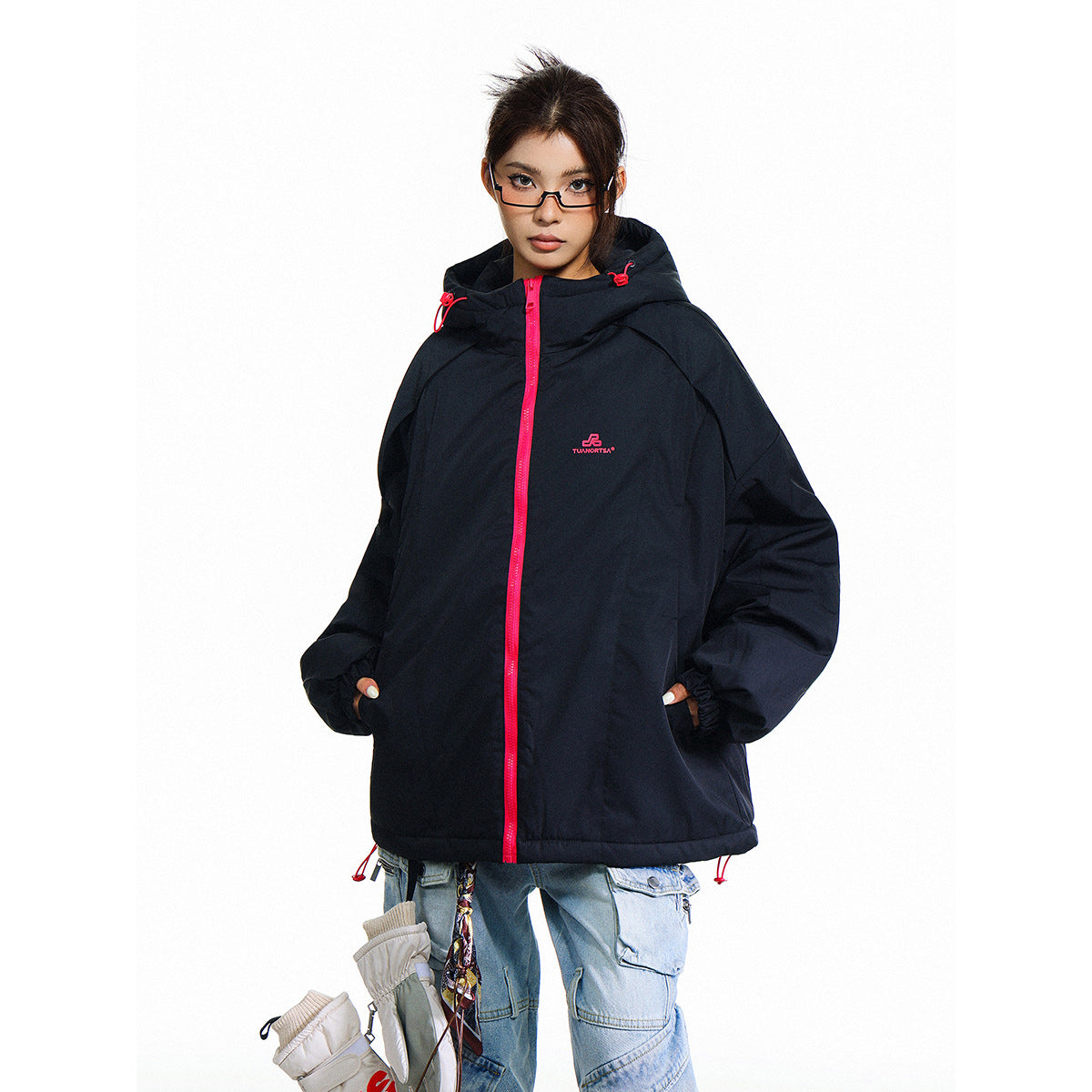 Model wearing a black oversized hooded jacket with a vivid pink zipper and drawcords, paired with light blue cargo jeans.