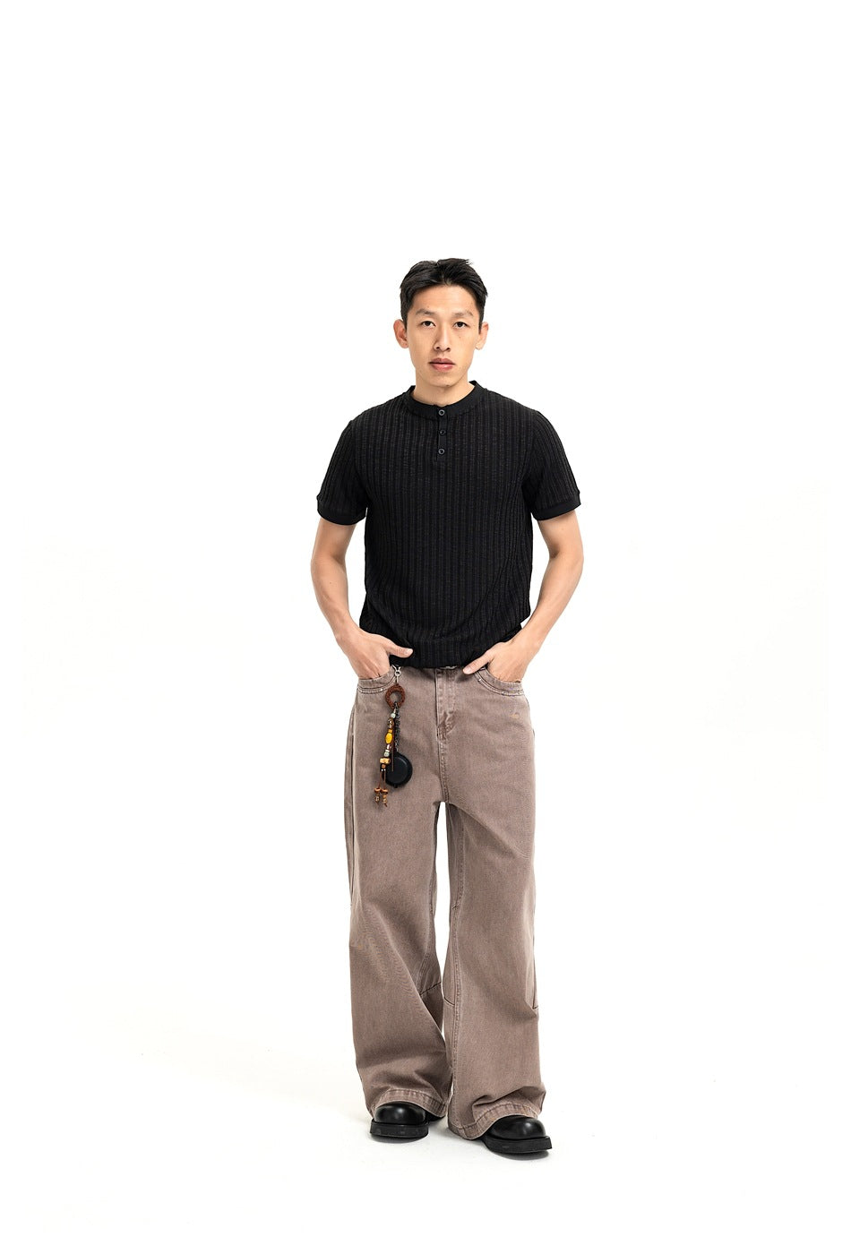 Man wearing a black ribbed short-sleeve henley shirt with taupe wide-leg trousers, shown from the front.