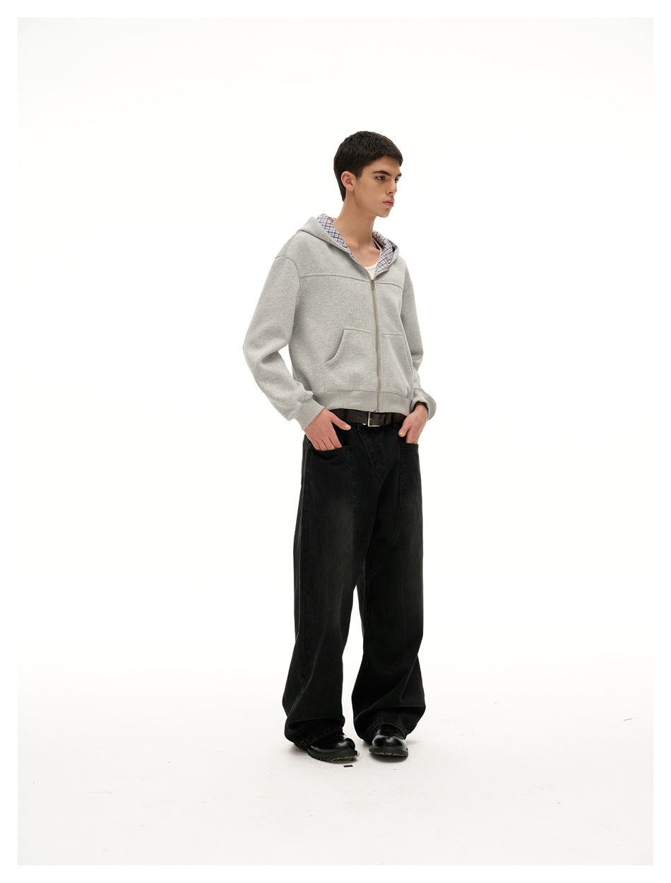 Model in a light gray zip-up hoodie with blue plaid hood lining and wide black pants, shown at a three-quarter angle.
