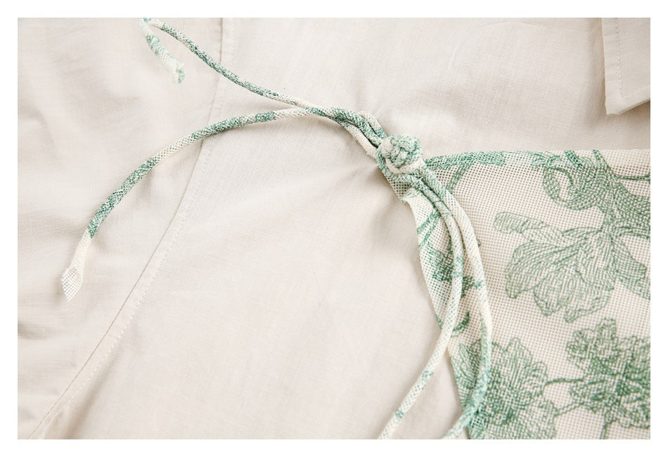Close-up of a knotted fabric tie beside the ivory shirt's green floral-patterned panel.