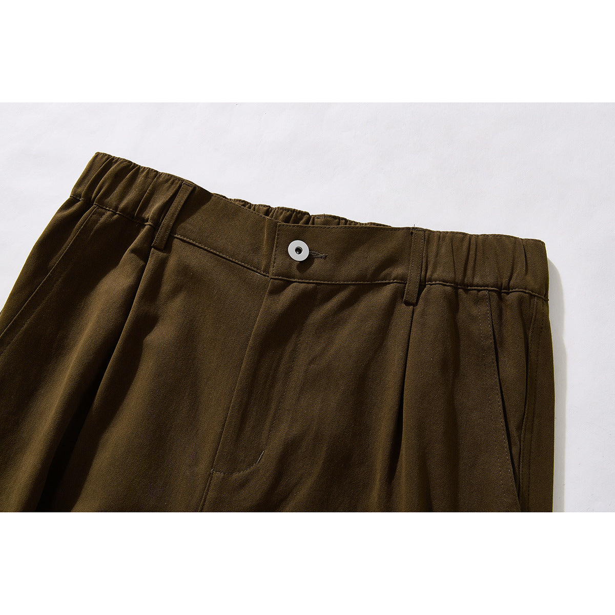 Close-up of dark brown trousers showing an elasticated waistband, button, belt loops and front pleats.