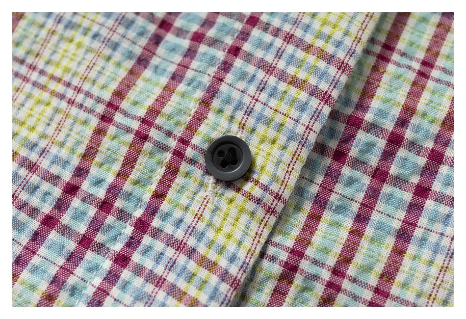 Close-up of a black button on a multicolor plaid shirt with burgundy, blue, green, and yellow checks.