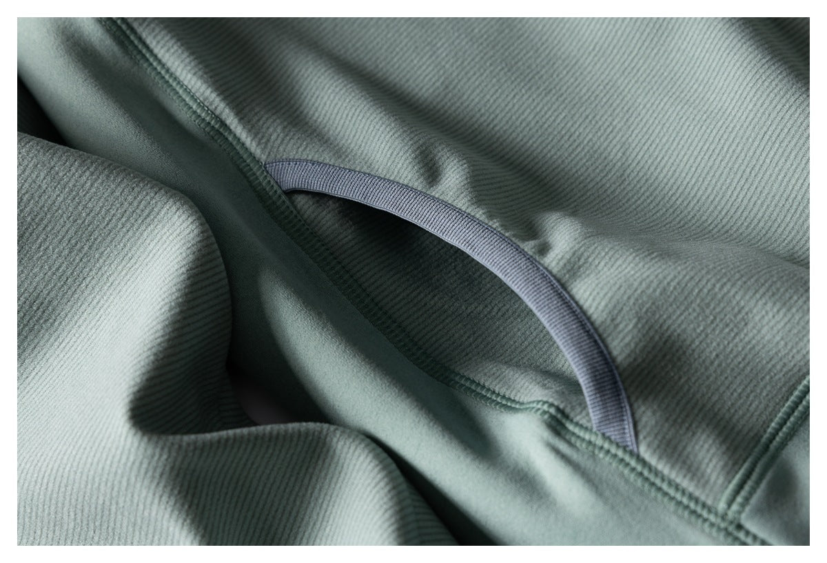 Close-up showing the sage-green jacket’s ribbed fabric, curved seam, and dark contrasting trim.