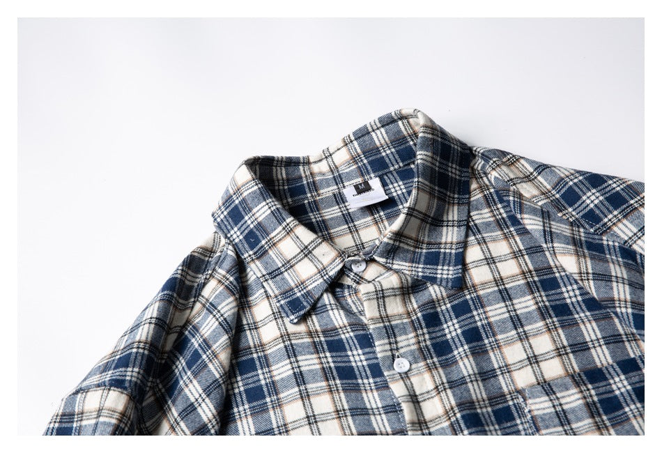 Close-up of a navy, cream, and tan plaid shirt collar and upper button placket, laid flat.