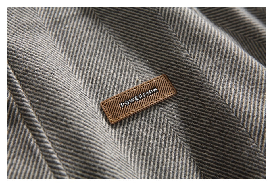 Close-up of a small brown rectangular lettering patch on the jacket's gray herringbone fabric.