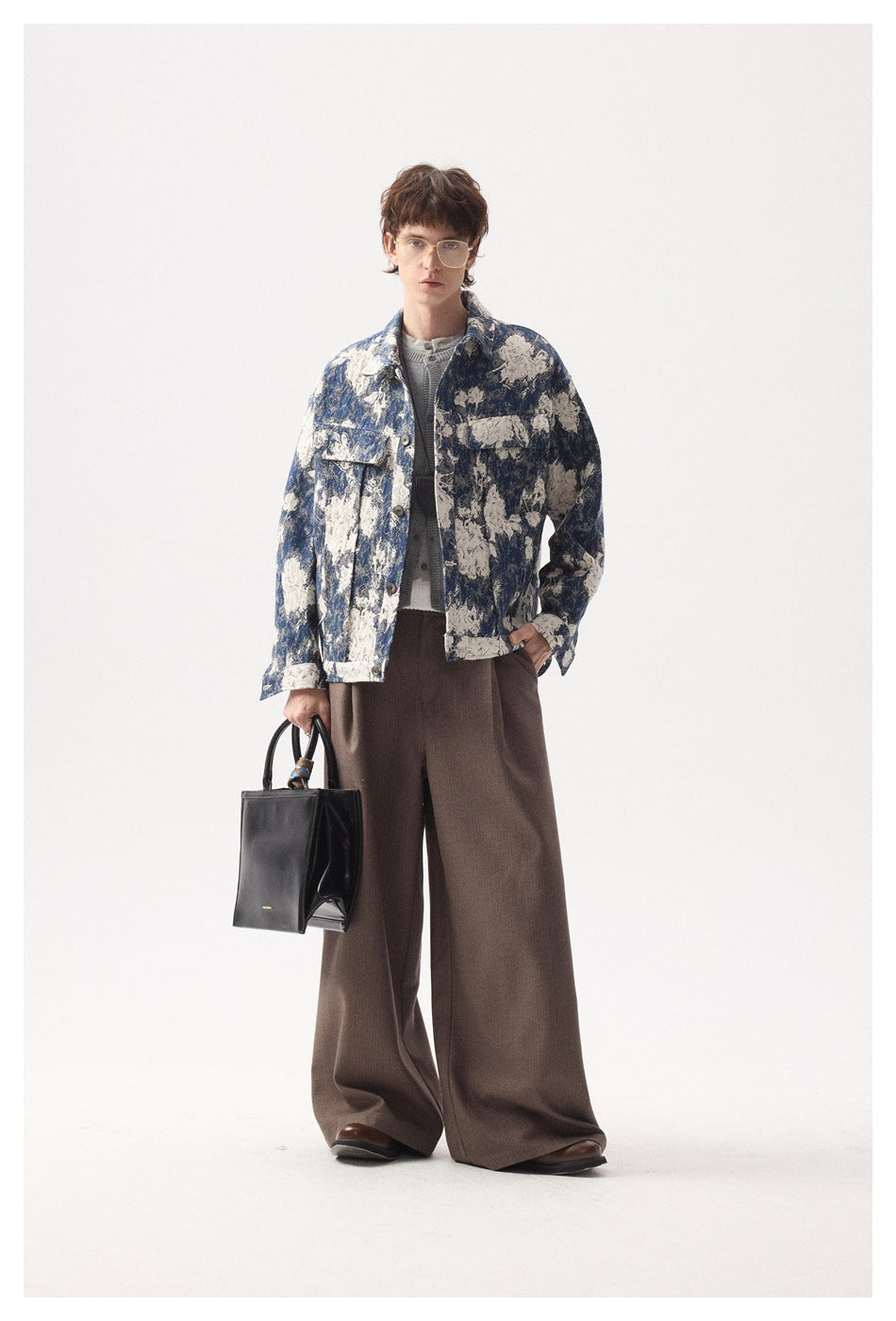 Model in a blue and cream floral jacket with one hand in pocket, brown wide-leg pants and a black tote bag